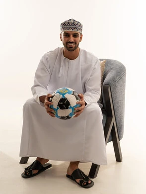 رجل عماني بالزي التقليدي يمسك كرة قدم