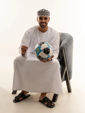 رجل عماني بالزي التقليدي يحمل كرة قدم