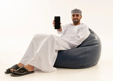 رجل عُماني يحمل هاتفاً ذكياً على مقعد محشو