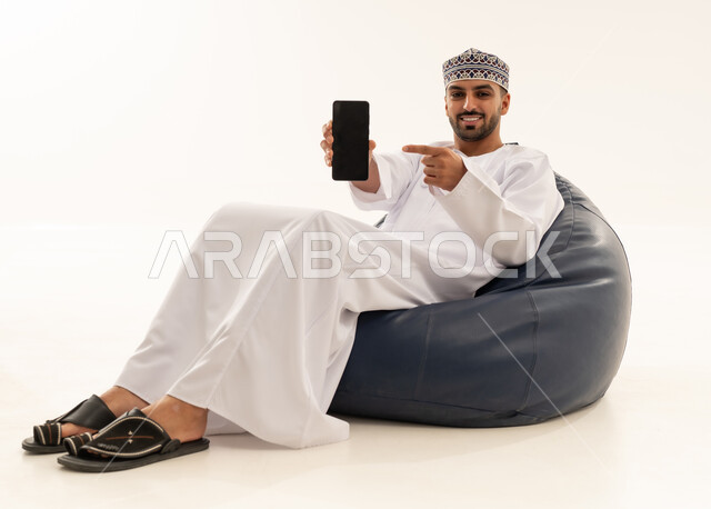 رجل عماني يشير إلى شاشة هاتف ذكي على خلفية بيضاء