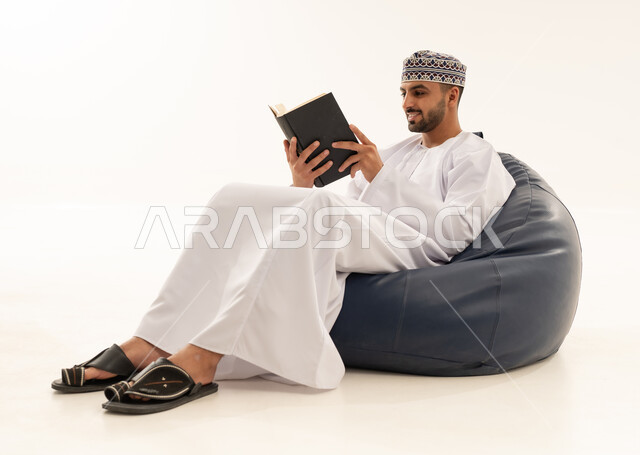 رجل عماني بالزي التقليدي يقرأ كتاباً في الاستوديو