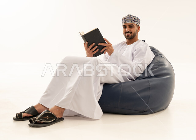 رجل عُماني بالزي التقليدي يقرأ كتاباً على مقعد مريح