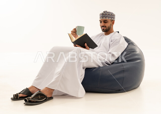 رجل عماني بالزي التقليدي يقرأ كتابا على كرسي مريح