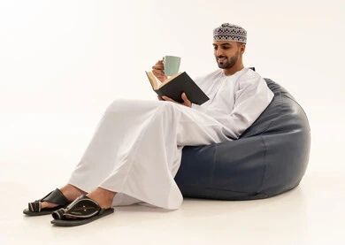 رجل عماني بالزي التقليدي يقرأ كتابا على كرسي مريح