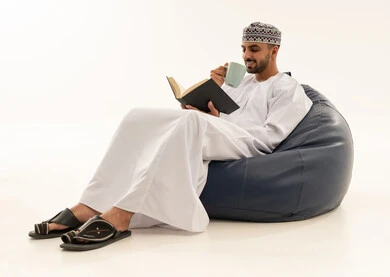 رجل عماني بالزي التقليدي يقرأ على مقعد محشو