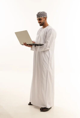 رجل عماني بالزي التقليدي يستخدم الحاسوب المحمول