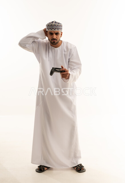 رجل عماني بالزي التقليدي يمسك بجهاز تحكم ألعاب