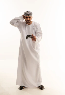 رجل عماني بالزي التقليدي يمسك بجهاز تحكم ألعاب