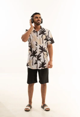 رجل سعودي يستمع للموسيقى بقميص صيفي ونقوش نخل