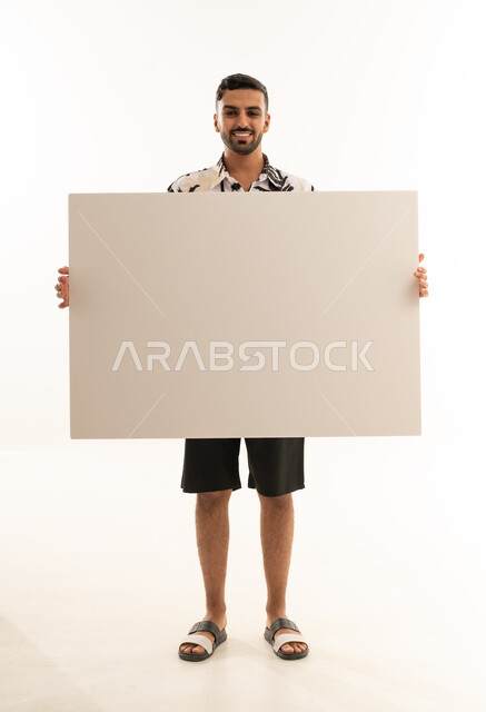 رجل سعودي يحمل لوحة بيضاء فارغة أمام خلفية بيضاء