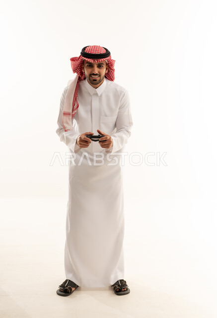 رجل سعودي بالثوب التقليدي يمسك جهاز تحكم ألعاب