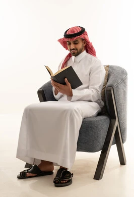 رجل سعودي بالثوب التقليدي يقرأ كتاباً في الاستوديو