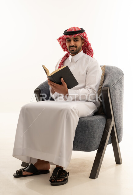 رجل سعودي بالزي التقليدي يقرأ كتاباً في استوديو