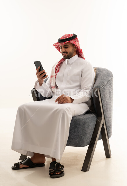 رجل سعودي بالثوب التقليدي يستخدم الهاتف الذكي