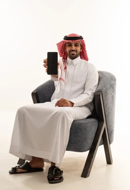رجل سعودي يحمل هاتف ذكي في استوديو بخلفية بيضاء