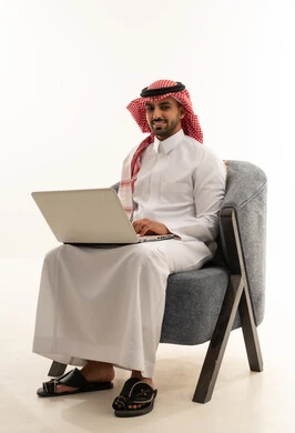 Saudi Man in Thobe Using Laptop on Modern Chair