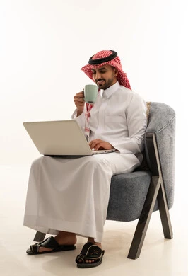 رجل سعودي يرتدي الثوب التقليدي يستخدم الحاسوب