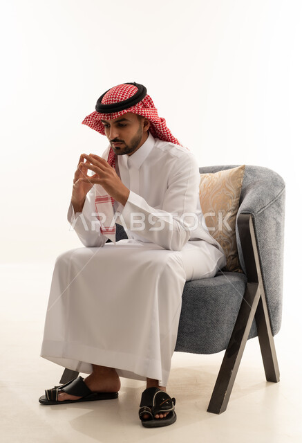 رجل سعودي بالزي التقليدي يجلس على كرسي رمادي