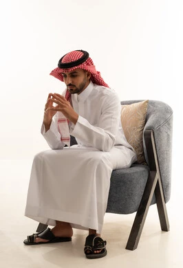 رجل سعودي بالزي التقليدي يجلس على كرسي رمادي