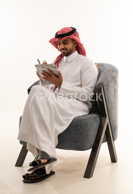 رجل سعودي بالزي التقليدي يكتب على لوحة ملاحظات