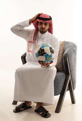رجل سعودي بالزي التقليدي يمسك كرة قدم