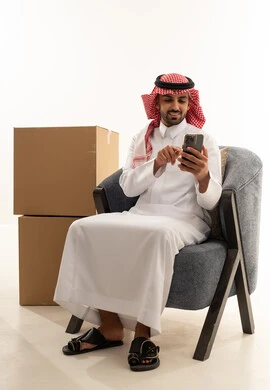 رجل سعودي يستخدم الهاتف الذكي بجانب صناديق شحن