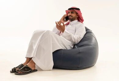 رجل سعودي بالثوب يتحدث بالهاتف على مقعد محشو