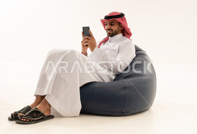 رجل سعودي بالثوب يستخدم الجوال على مقعد مريح