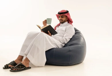 رجل سعودي يقرأ كتاباً على مقعد محشو خلفية بيضاء