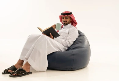 Saudi Man in Traditional Thobe Reading on Beanbag