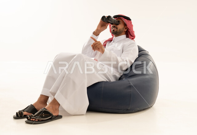 رجل سعودي بالثوب والشماغ يستخدم المنظار بخلفية بيضاء