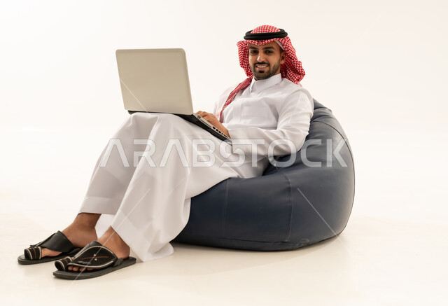 Saudi Man in Traditional Thobe Using Laptop on Beanbag