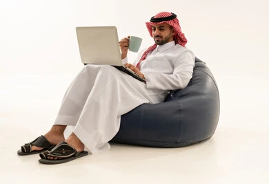 رجل سعودي يستخدم اللابتوب على مقعد استرخاء بخلفية بيضاء