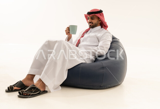 رجل سعودي بالثوب التقليدي يجلس على كرسي استرخاء