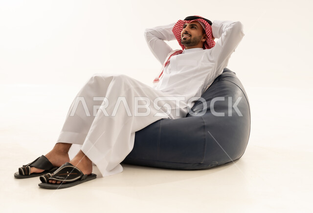 رجل سعودي بالثوب التقليدي يسترخي على مقعد محشو