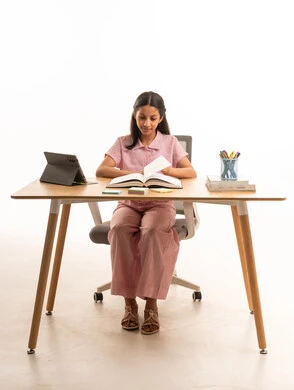 فتاة سعودية تقرأ كتاباً على المكتب بخلفية بيضاء