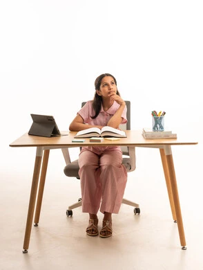 Saudi Girl Thinking at Desk with Book and Tablet