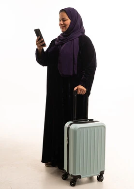 امرأة عربية مع حقيبة سفر تستخدم الهاتف الذكي