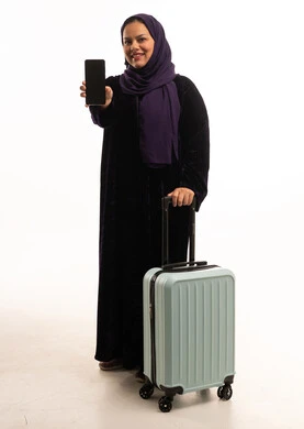 امرأة سعودية مع حقيبة سفر تحمل هاتفاً ذكياً خلفية بيضاء