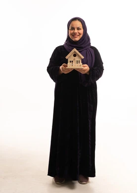 امرأة سعودية بعباية تحمل مجسم منزل خشبي