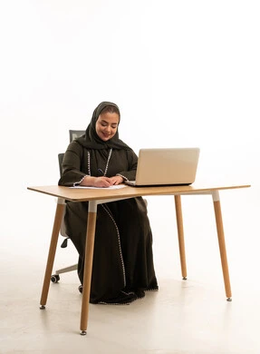 سيدة أعمال إماراتية تعمل على لابتوب بخلفية بيضاء