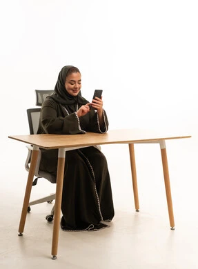 امرأة سعودية بالعباءة تستخدم الهاتف الذكي في المكتب