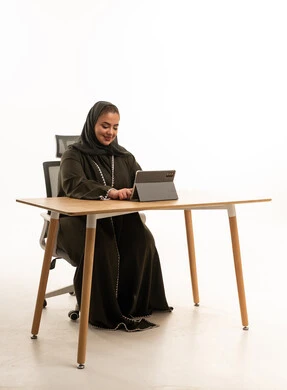 سيدة أعمال إماراتية تعمل على جهاز لوحي بالعباءة