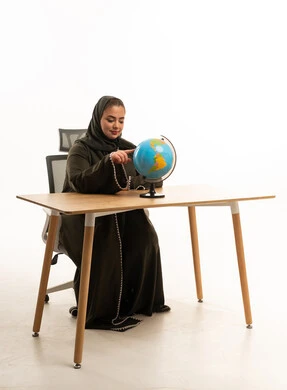 امرأة سعودية بالعباءة تشير إلى مجسم الكرة الأرضية