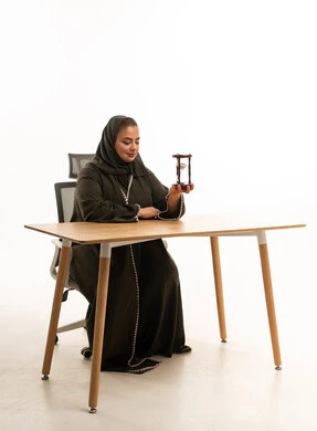 امرأة سعودية بالعباءة تحمل ساعة رملية على المكتب