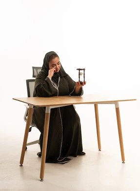 امرأة سعودية بالعباءة تحمل ساعة رملية في مكتب