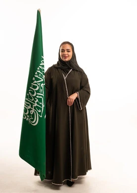 امرأة سعودية بالعباءة مع علم المملكة