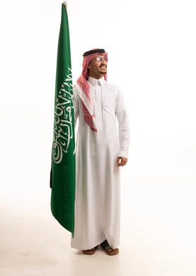 رجل سعودي بالزي التقليدي يحمل العلم الوطني