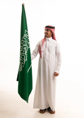 رجل سعودي بالزي التقليدي يحمل علم المملكة العربية السعودية