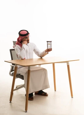 رجل سعودي بالثوب التقليدي يمسك ساعة رملية